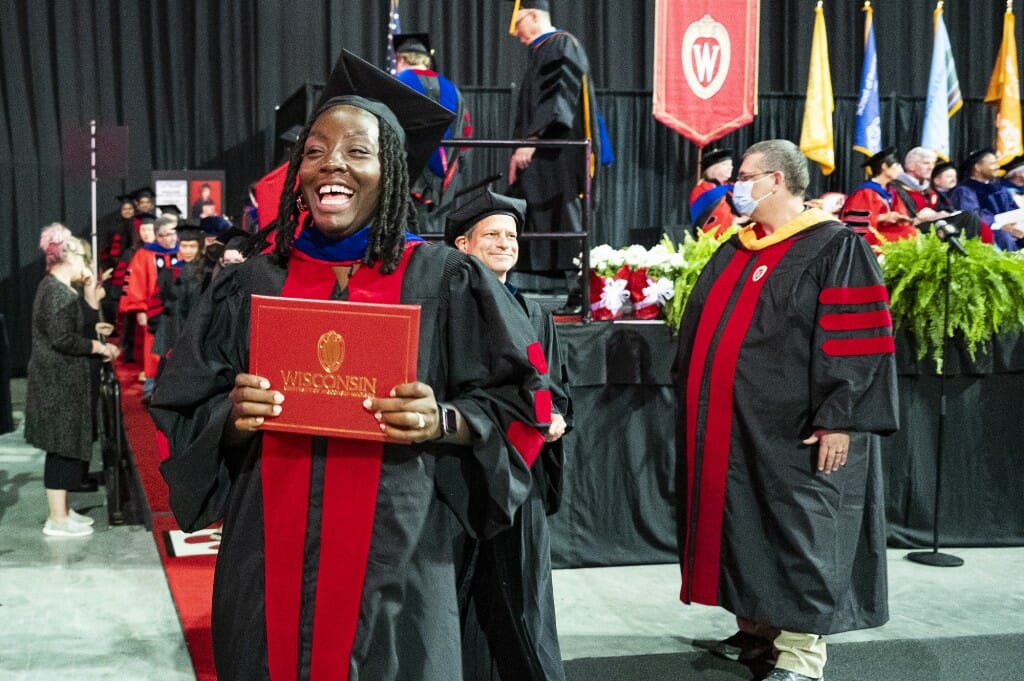 Person in cap and gown holding diploma cover and waving