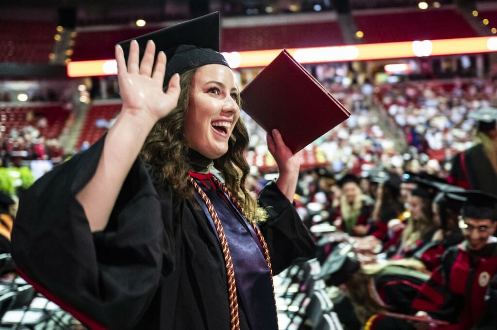 Person in cap and gown smiling and waving