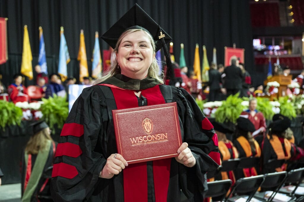 Smiling person in cap and gown holding red diploma cover