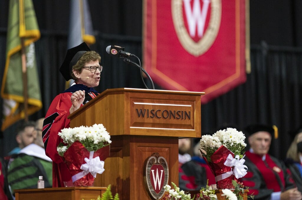 Blank in academic hood and robe speaking at podium