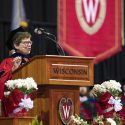 Blank in academic hood and robe speaking at podium