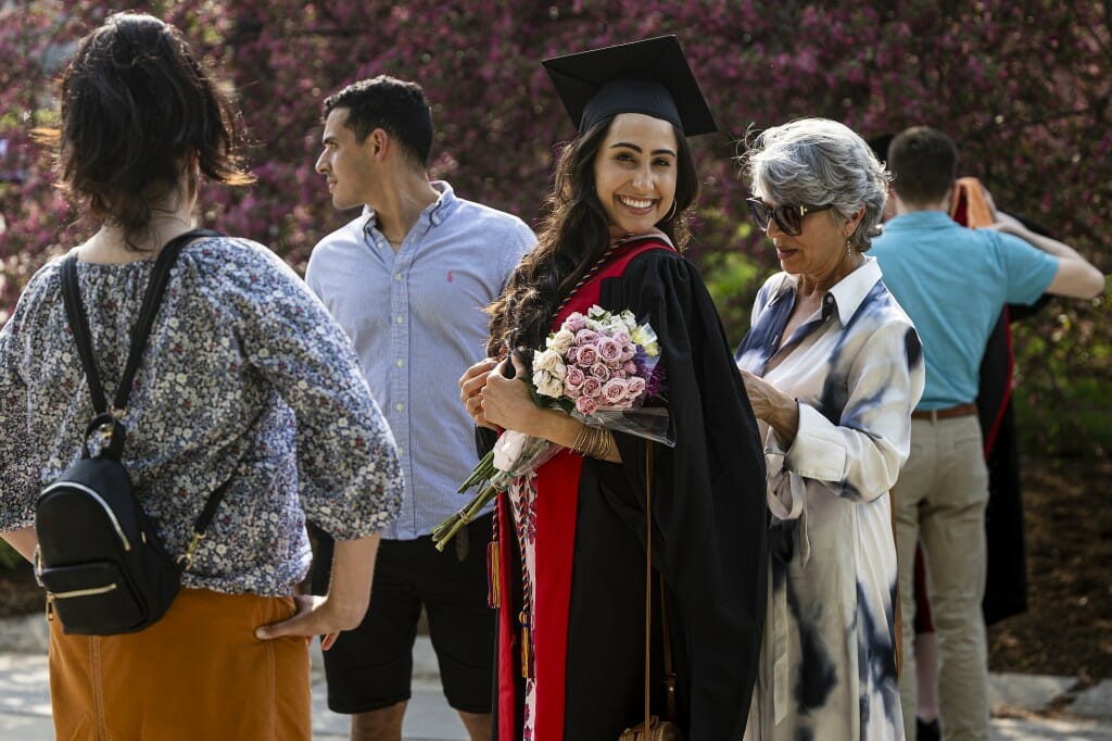 Person in cap and gown holding flowers while another person reaches behind her