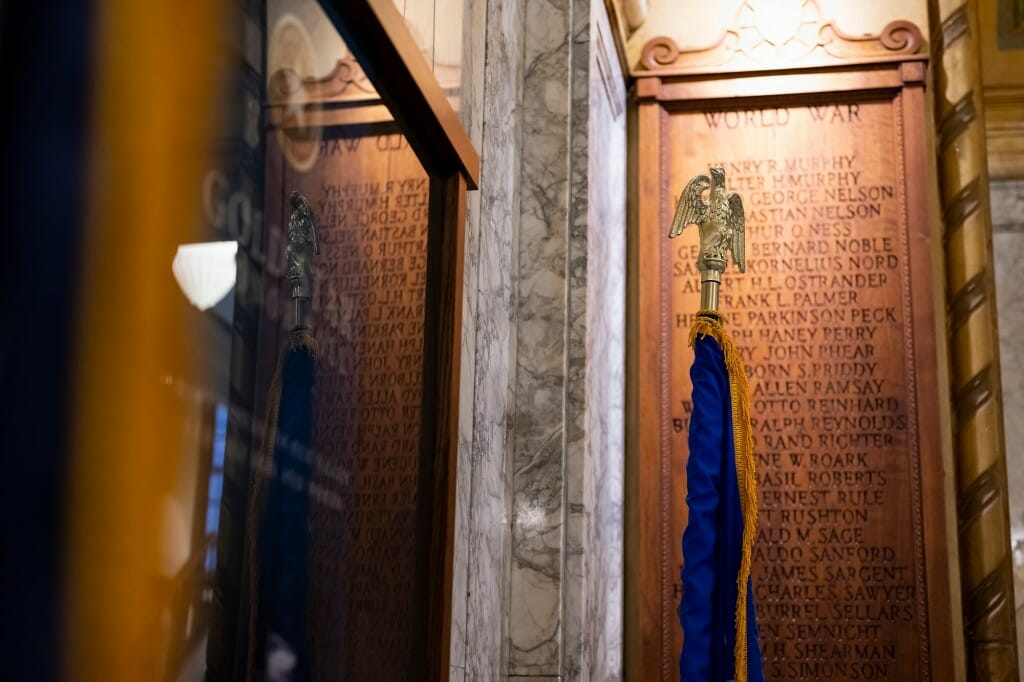 Closeup of flag in front of wooden plaque with names carved in it