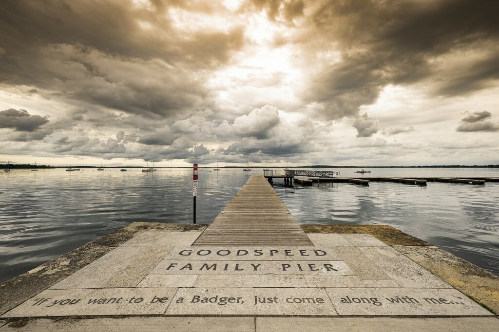 View from short of pier extending into lake under dramatic gray and white cloudscape after a storm