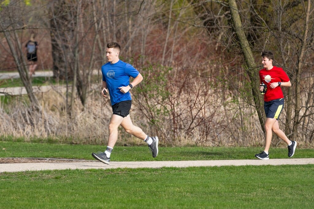 Two men jogging down a path past still-brown vegetation