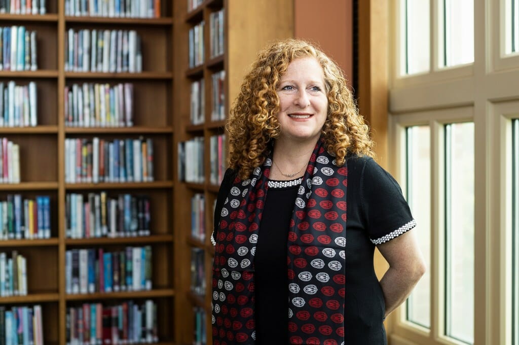 Portrait of Mnookin standing in front of a bookcase and a window