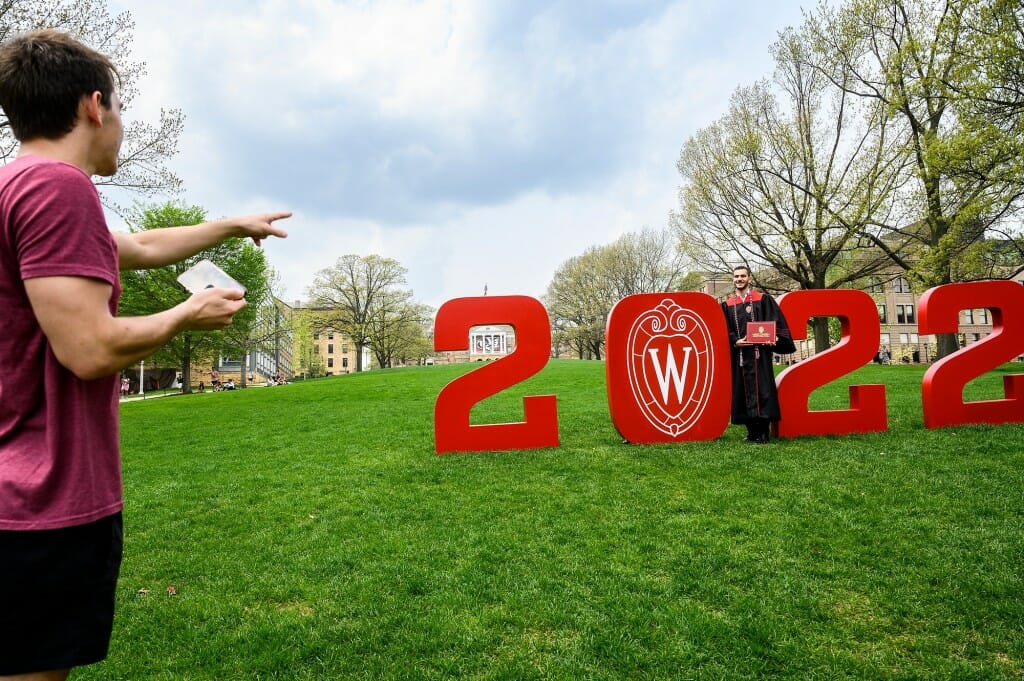 Soon-to-be-graduate Canaan Odeh poses while wearing his graduation gown with the numerals “2022” while sophomore Michael Nichols directs his photo.