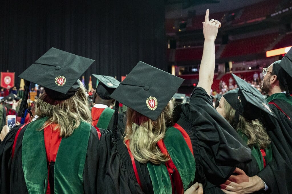 People in caps and gowns seen from behind with arms raised