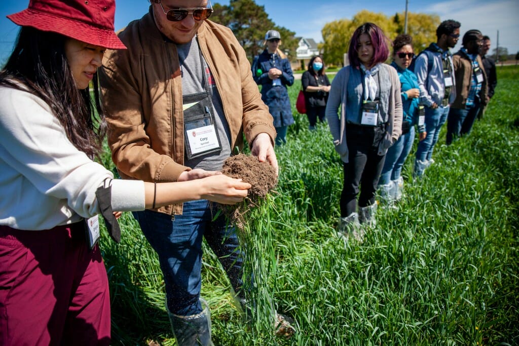 Members of the bus tour group examine a clump of roots in a crop field.