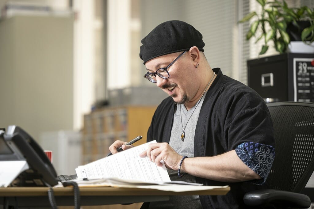 Calyx sitting at a desk reading papers