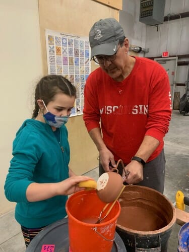 Mick and Cora holding a pot over a bucket of water