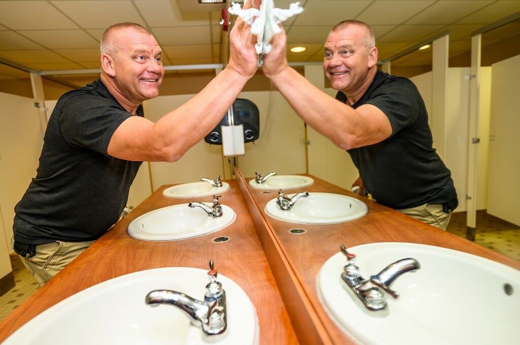 MacWilliams wiping a mirror over a sink in a restroom