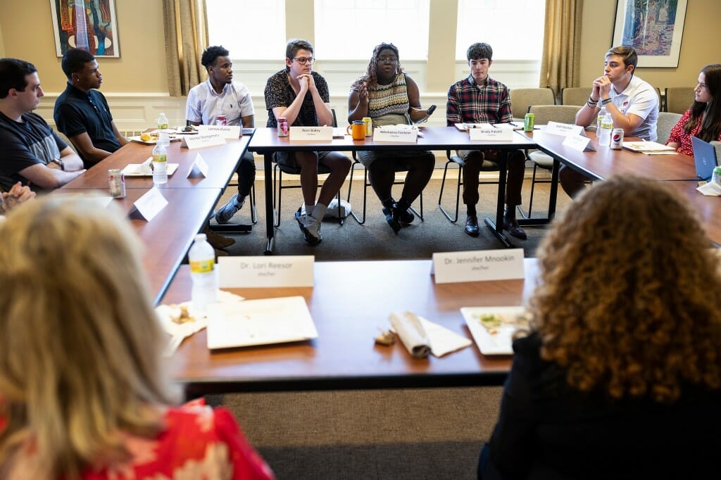 A group of students sitting around a table in a conference room while Mnookin and Reesor listen