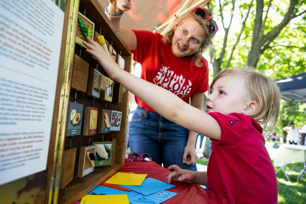 A child reaching to turn a tile in a wooden grid while a smiling adult watches