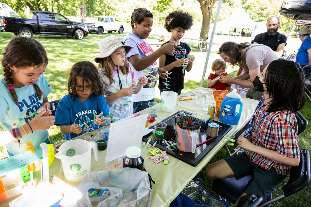 Several children standing at a table with small components of a science experiment