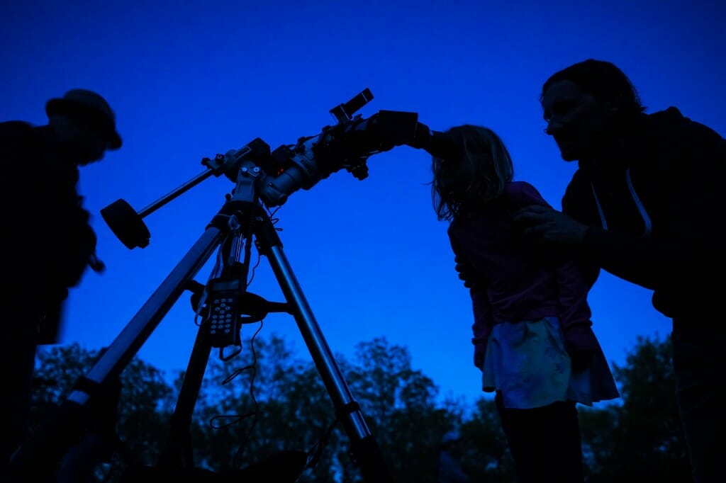 Silhouetted figure leaning toward eyepiece of telescope