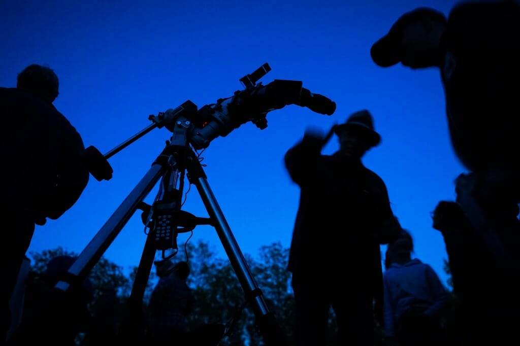 Silhouetted figure in a hat pointing at a telescope