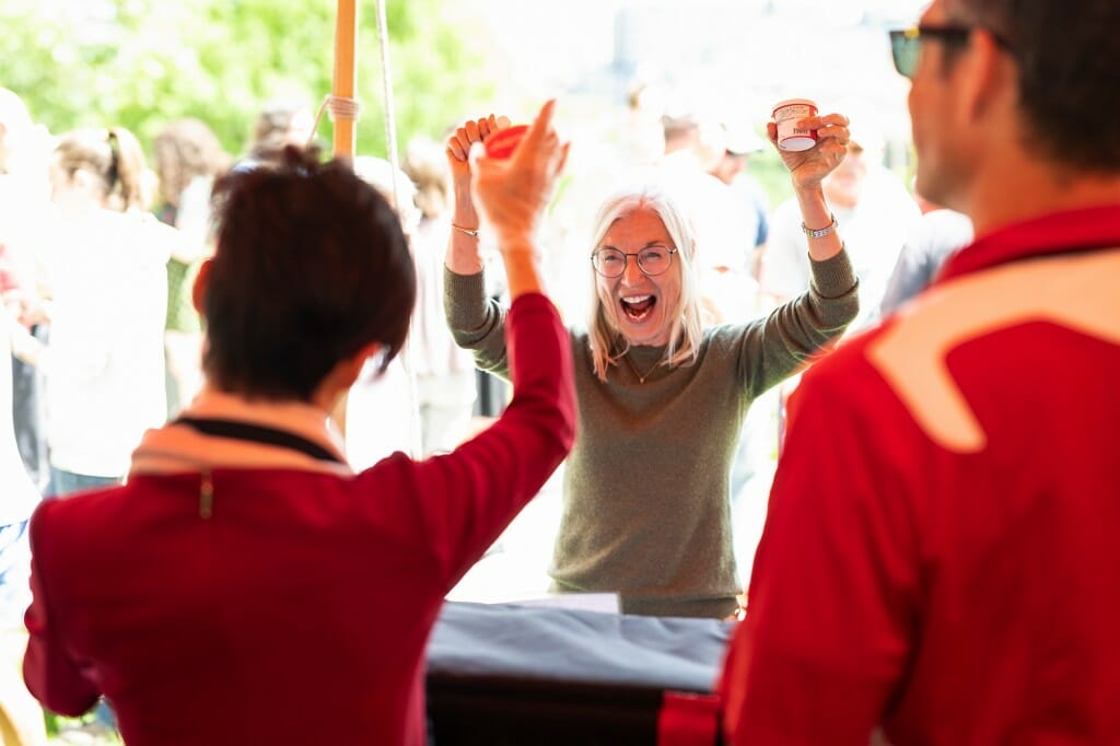 A smiling person with arms raised looks into the tent