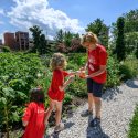 A girl hands flowers to a woman, in a garden.