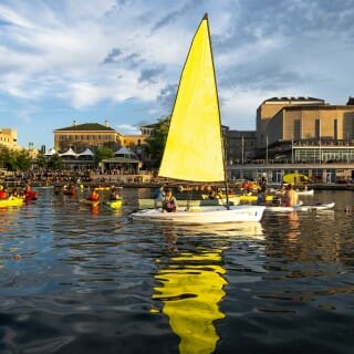 A sailboat with a bright yellow sail floats on blue water, other boats in the background.