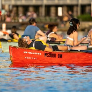 A man stretches out and sleeps in his red canoe, dog on his lap.