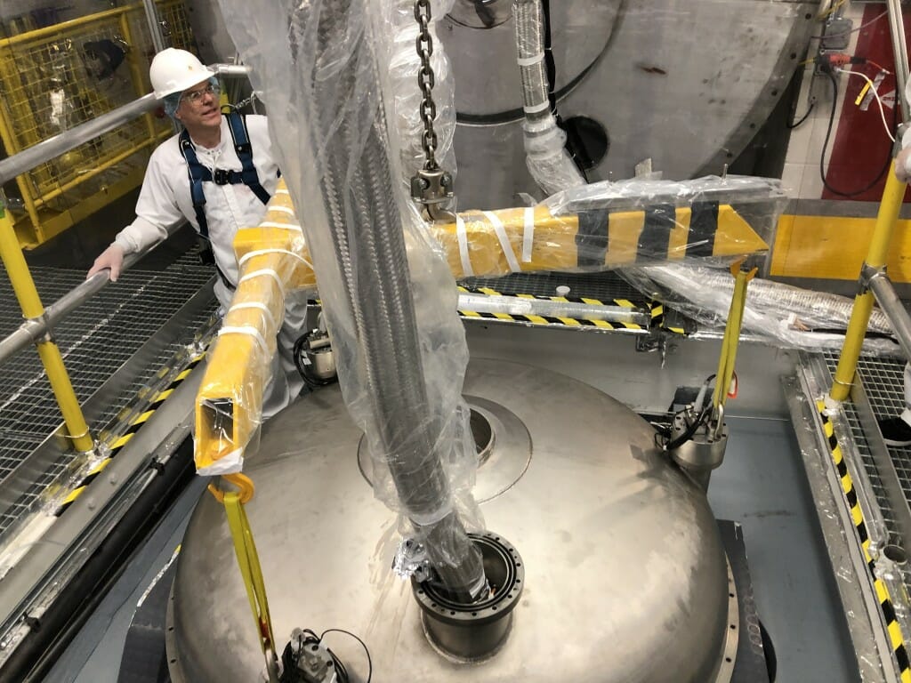 Jeff, wearing hardhat, standing next to large cryostat head