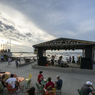 People sit at tables on the Terrace, listening to a band facing the lake.