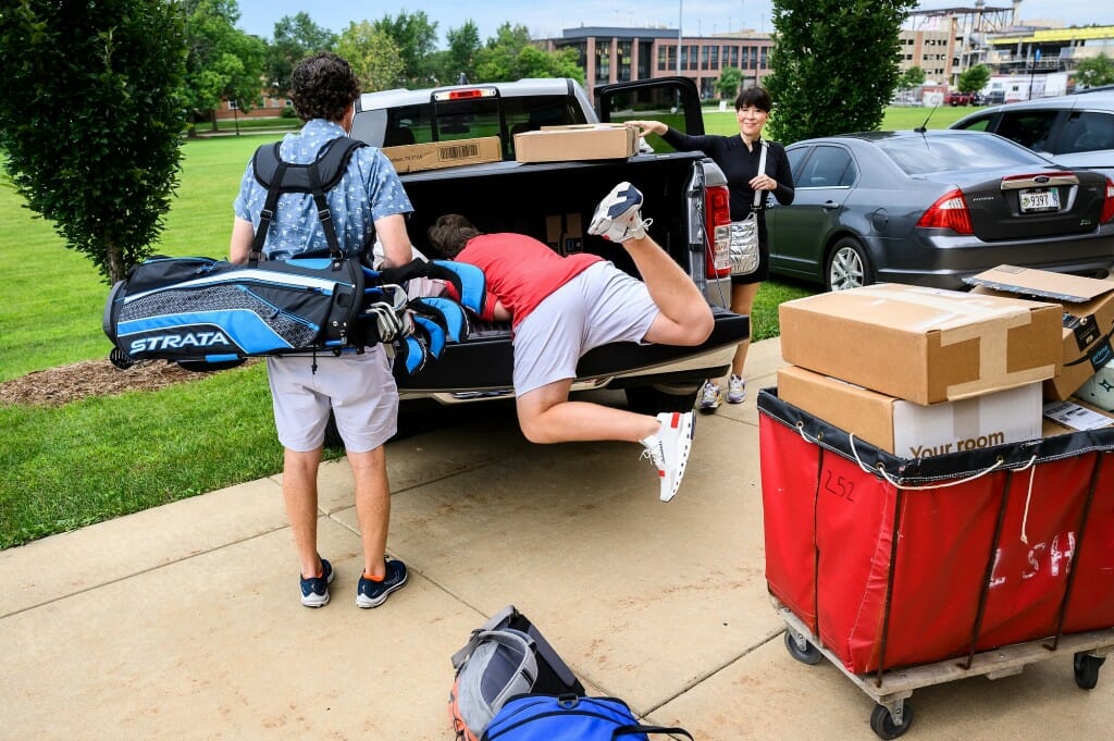 First-year student Charlie Campbell from Dallas, Texas, dives into the back of a pick-up truck to pull out boxes while his parents look on.