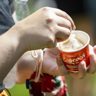 A hand holding a spoon scoops ice cream out of a paper dish.