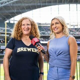 Chancellor Mnookin wears a navy blue Brewers shirt and talks into a microphone during an interview with a woman who wears a light blue shirt and jeans