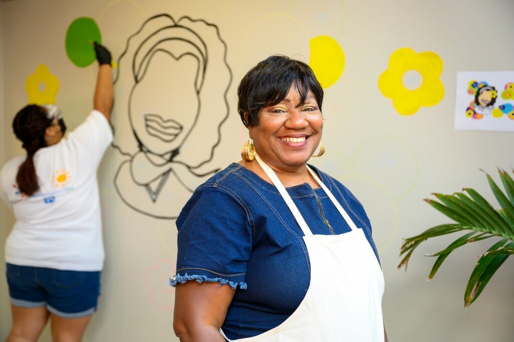 A woman stands in front of a sketch for a mural, that's unfinished.