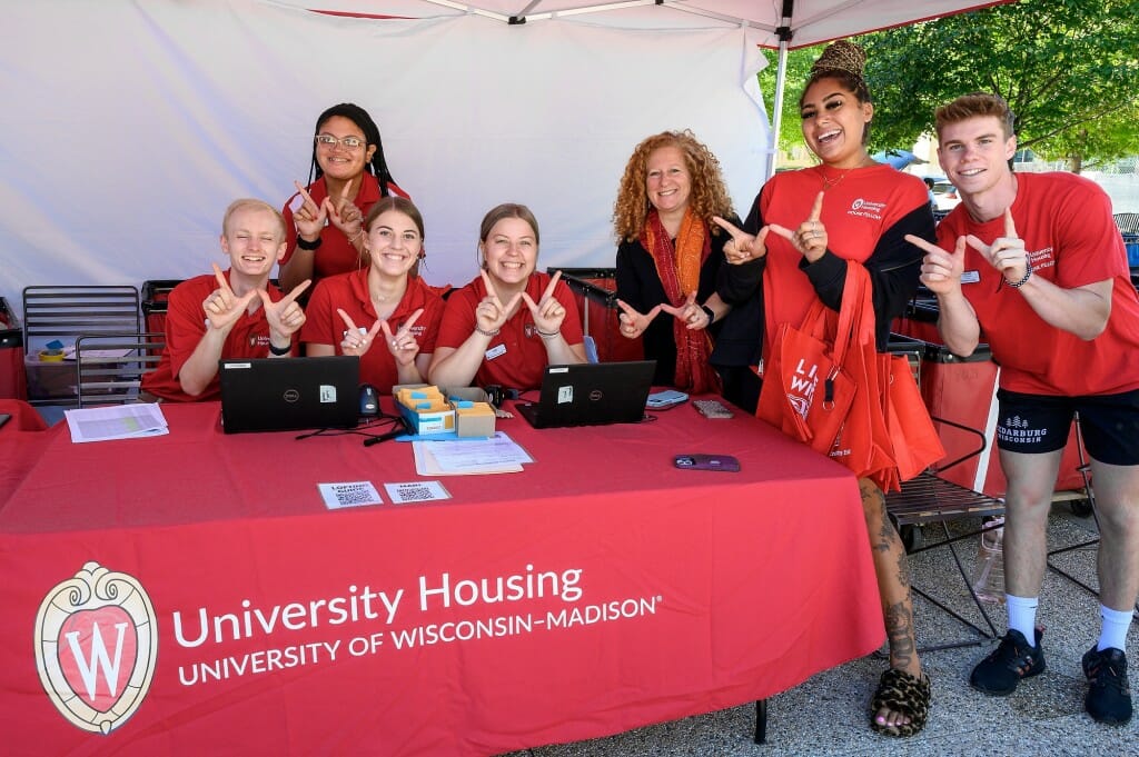 A group of people smile at the camera and hold up the W hand signal.