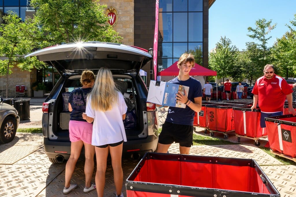 A group of people take stuff out of the back of a van and put it into a red card.