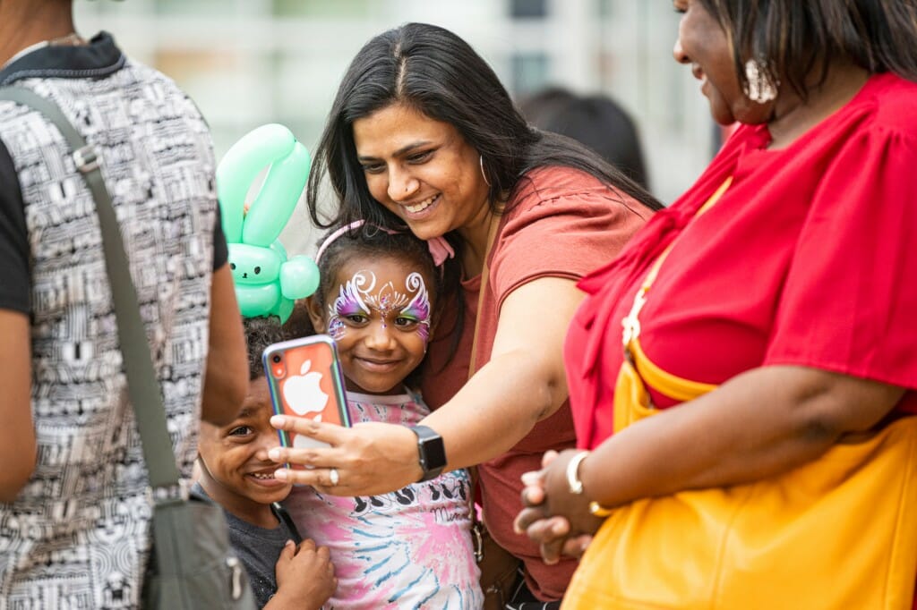 A woman takes a selfie with two children wearing facepaint.