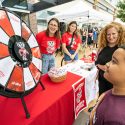 A boy stands at a spinning prize wheel as a woman smiles at him, and others in the background too.