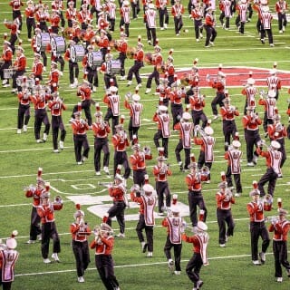 Band members wearing red and black march on the football field.