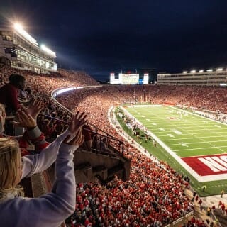 A young fan claps in the foreground, the lit-up football field is visible in the background.