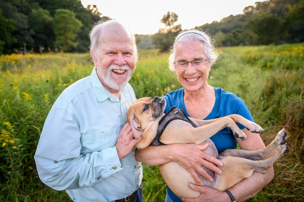 A couple pets and holds a small brown dog.