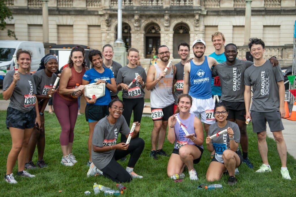 A group of runners stand on a lawn and hold up their 