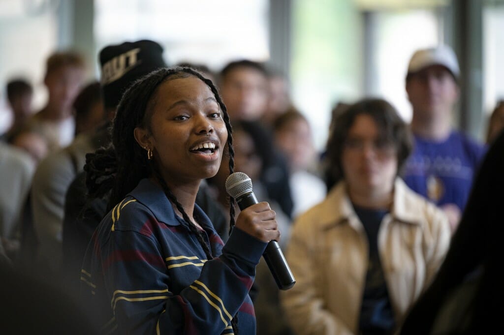 A woman speaks at a microphone as people listen.