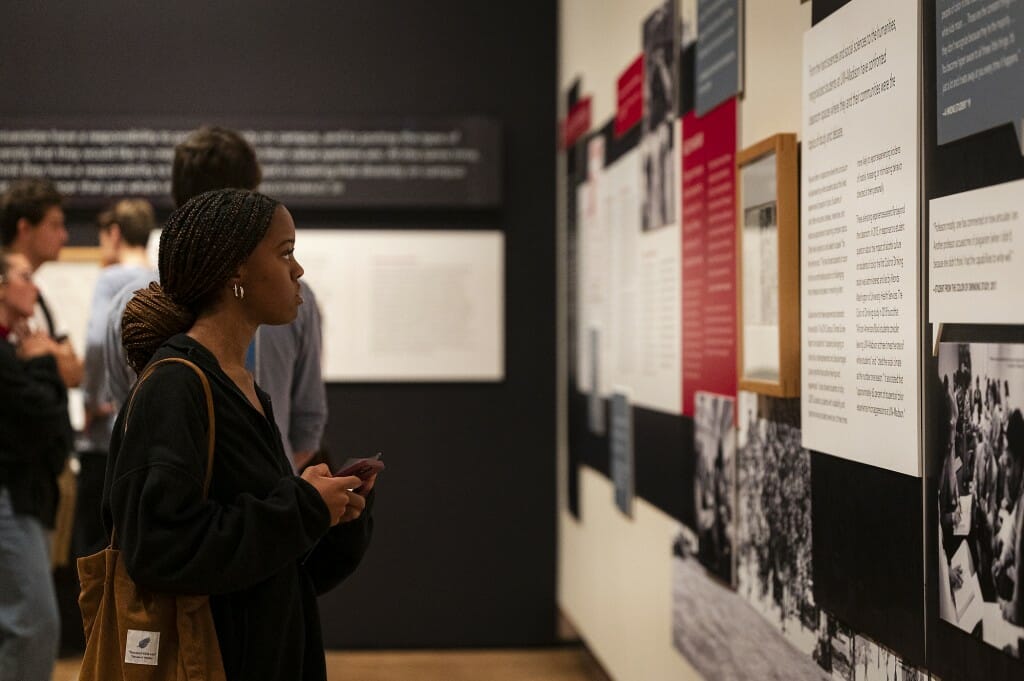 A woman stands alone, staring at an exhibit on the wall.