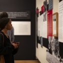 A woman stands alone, staring at an exhibit on the wall.