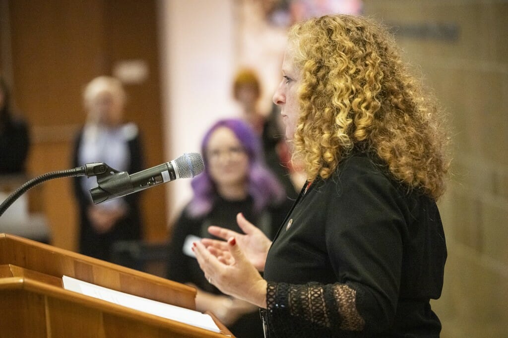 Chancellor Jennifer Mnookin faces left, speaking into a microphone and gesturing with open palms.