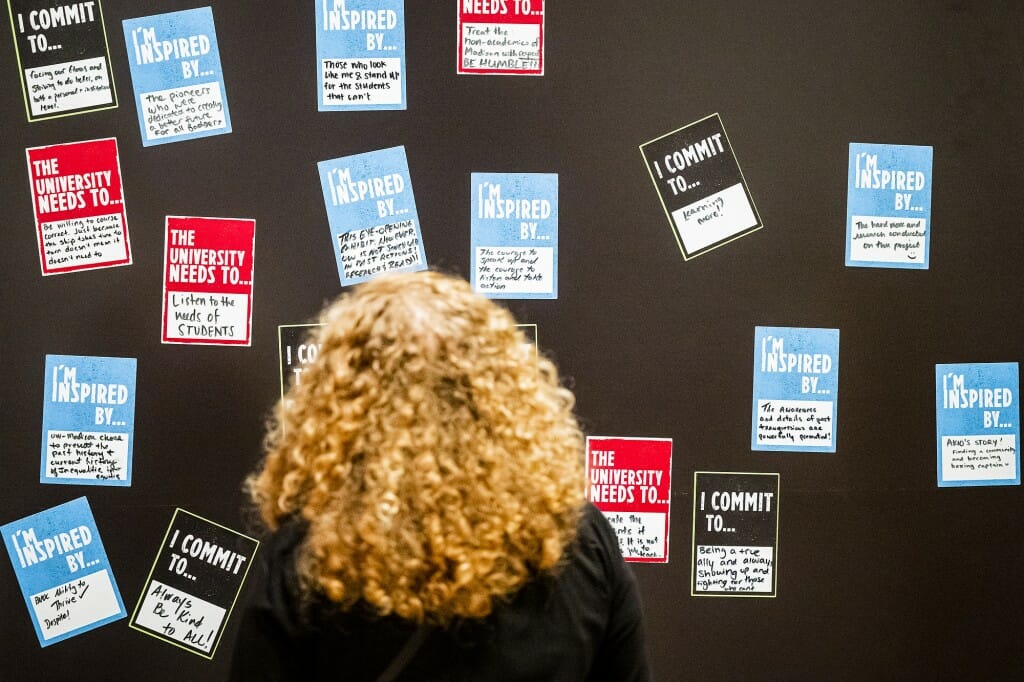 Chancellor Jennifer Mnookin faces away from the camera toward an exhibit wall covered in hand-written notes left by exhibit attendees.