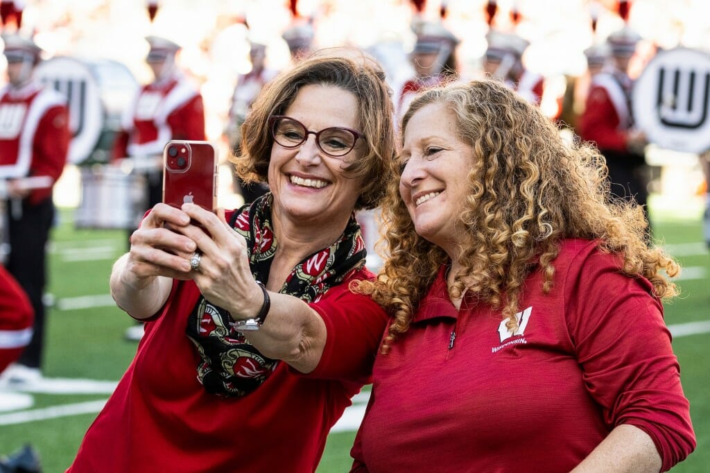 Sarah Schutt, executive director of the Wisconsin Alumni Association, uses her cellphone to take a selfie with UW–Madison Chancellor Jennifer Mnookin during halftime.