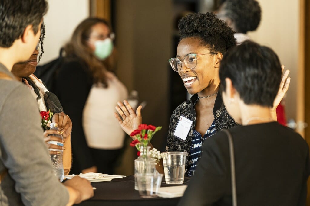 Amadi Ozier speaks with a smile on her face to a group gathered around a cocktail table.