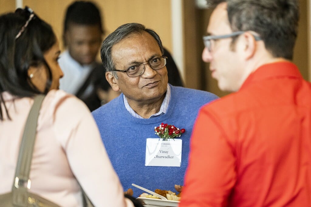 Vinay Dharwadker listens to colleagues around a cocktail table.