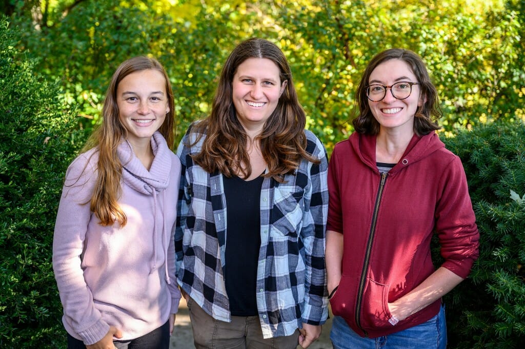 Three women stand and smile at the camera.