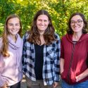 Three women stand and smile at the camera.