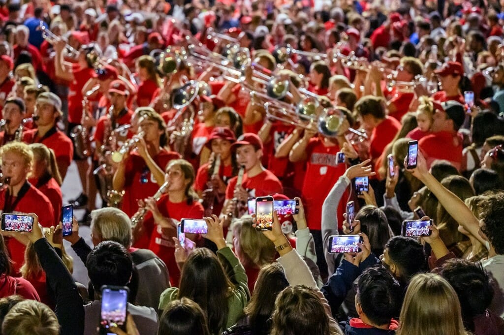 Homecoming parade spectators film the UW Marching Band with their phones as the band plays a final song at the end of State Street during the Homecoming Parade.